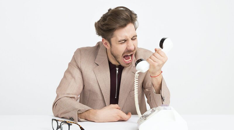 man wearing brown suit jacket mocking on white telephone