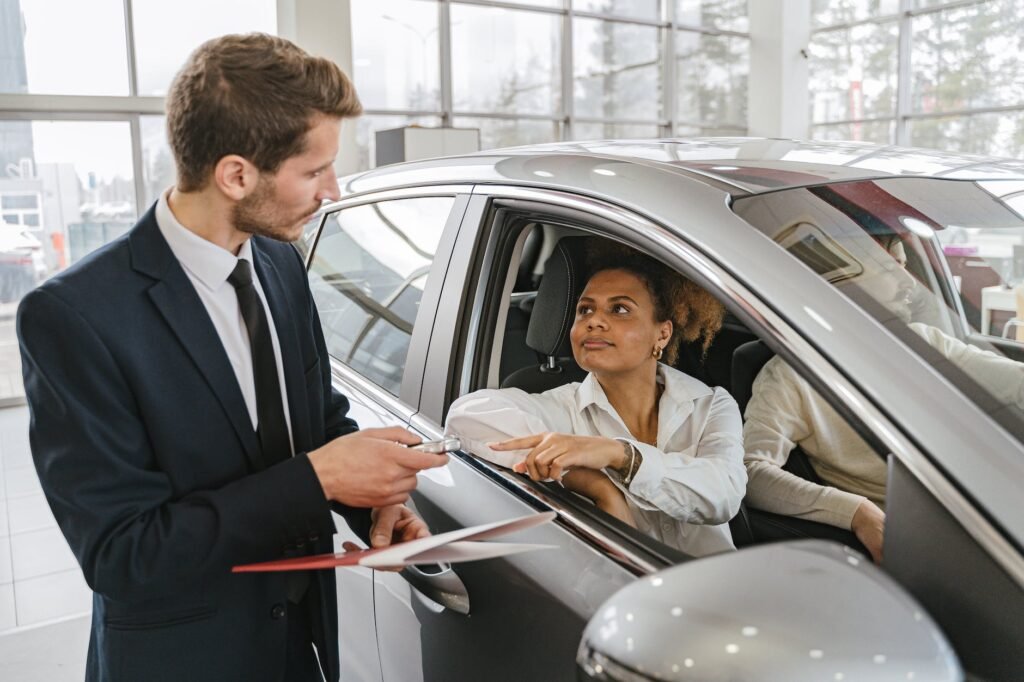 car dealer handing in keys to a woman sitting in a new car