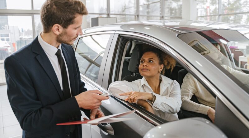 car dealer handing in keys to a woman sitting in a new car